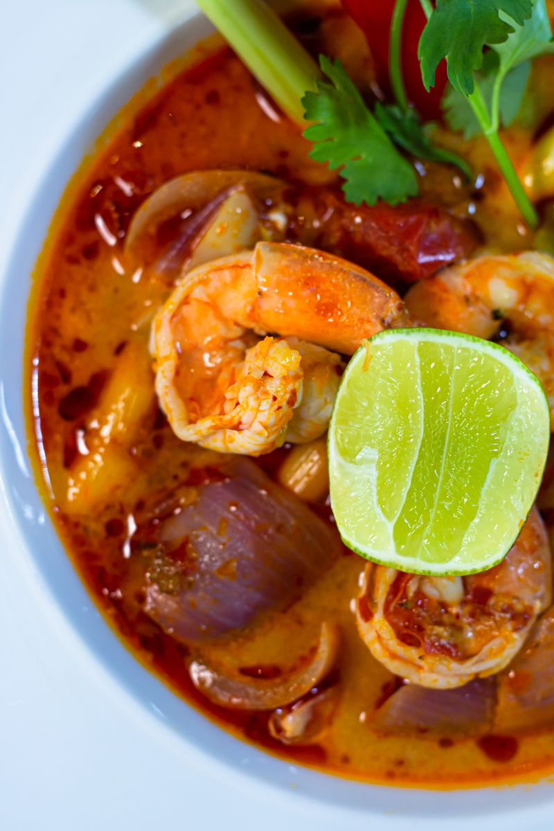 Authentic Thai Tom Yum soup with shrimp, lime, and herbs in a rich broth, showcasing vibrant flavors and colors.
