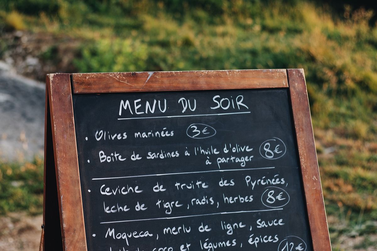 Chalkboard menu stand listing French dishes and prices in an outdoor setting.