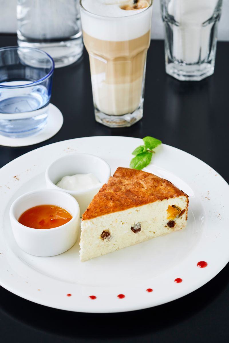 Cheesecake with sauces on a plate, served with latte and water.