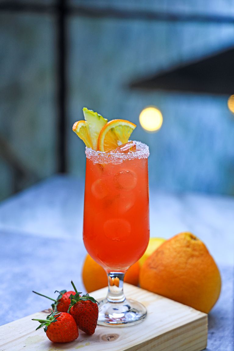 Chilled strawberry and orange cocktail with fresh fruit garnish on a wooden board.