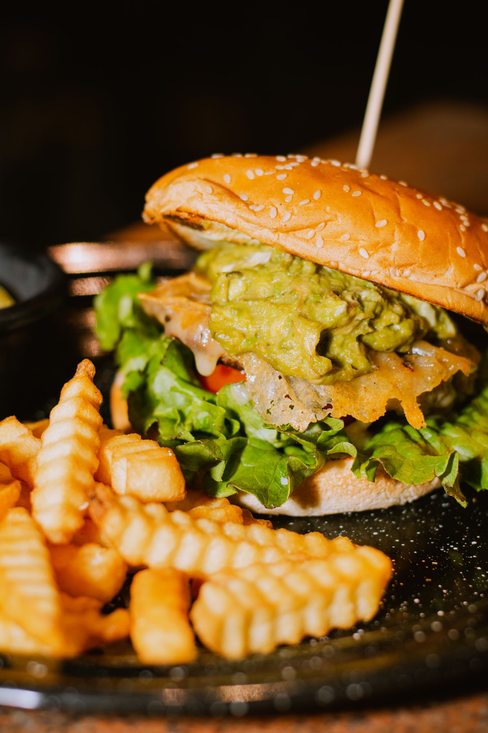 Close-up of a burger topped with guacamole and served with crinkle-cut fries.