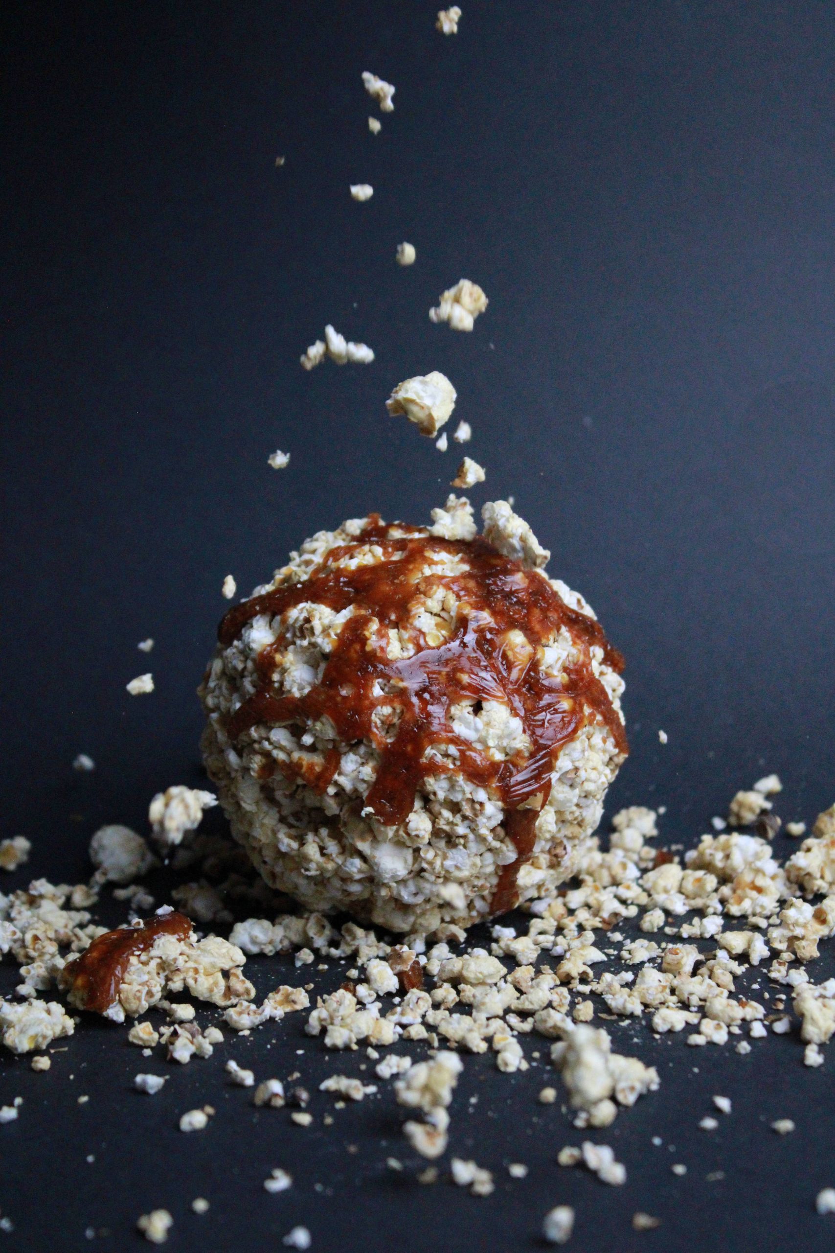 Close-up of a caramel-drizzled popcorn ball against a black background, capturing motion.