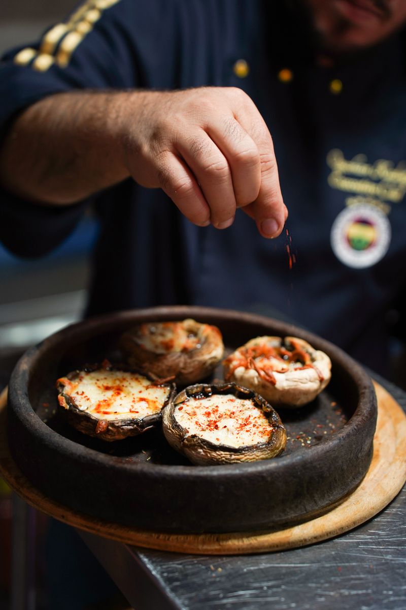 Close-up of a chef seasoning stuffed mushrooms in a Gökçeada taverna, capturing the essence of culinary artistry.