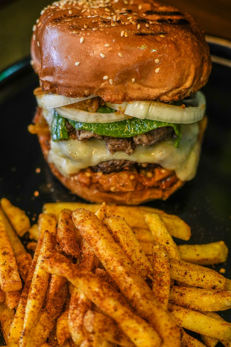 Close-up of a delicious hamburger with melted cheese and fries on a dark plate.