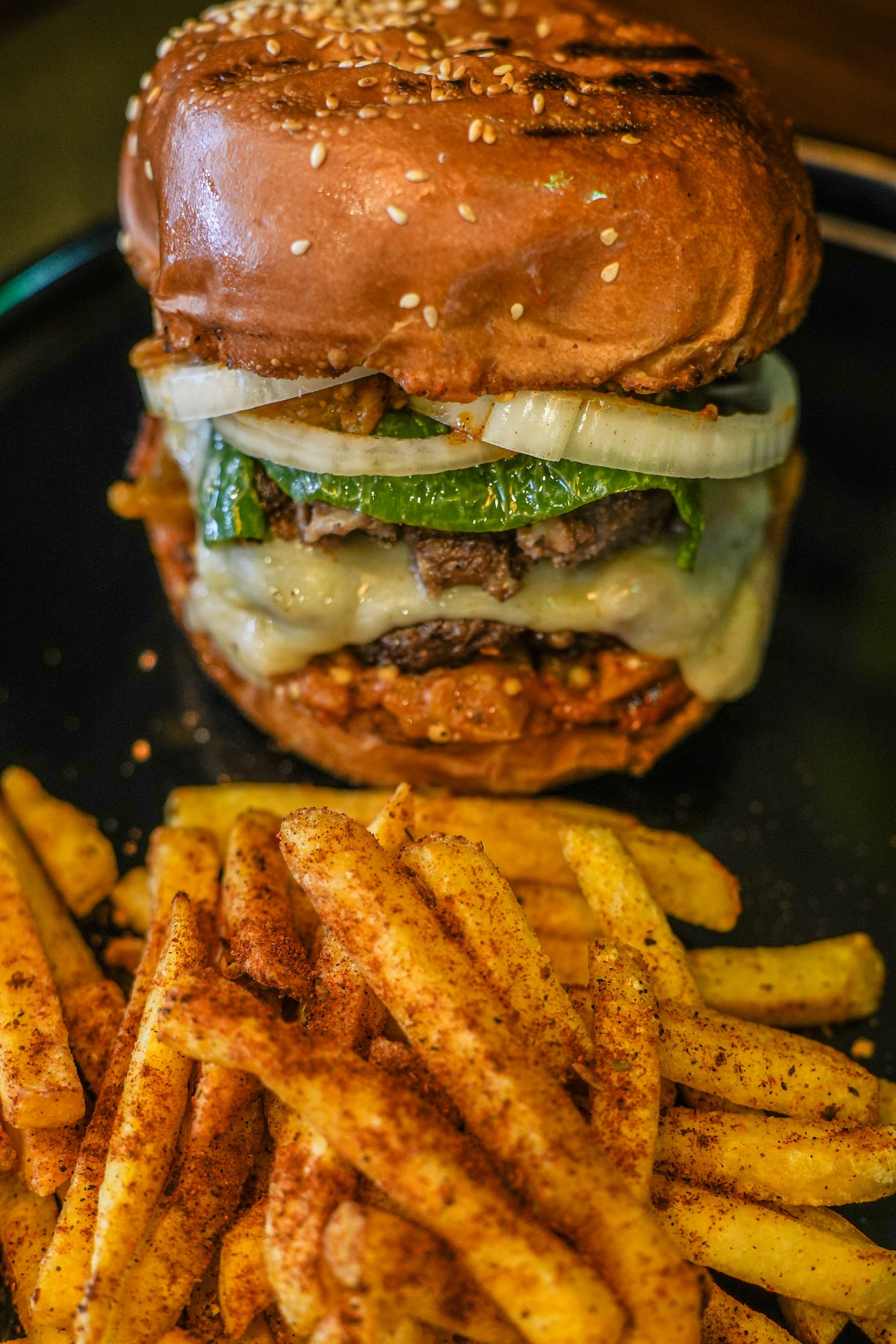 Close-up of a delicious hamburger with melted cheese and fries on a dark plate.