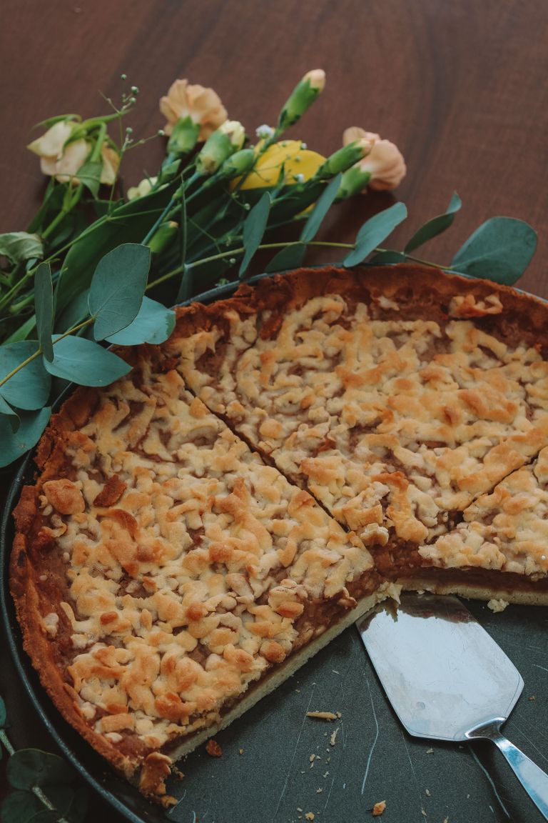 Close-up of a freshly baked apple pie next to a floral bouquet on a wooden table.