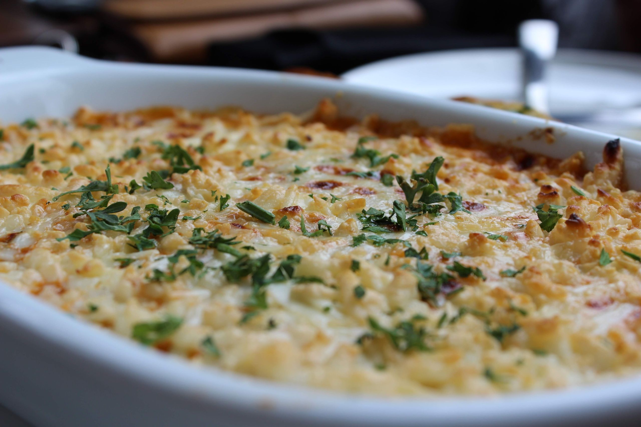 Close-up of a golden baked casserole dish topped with herbs, perfect for a comforting meal.