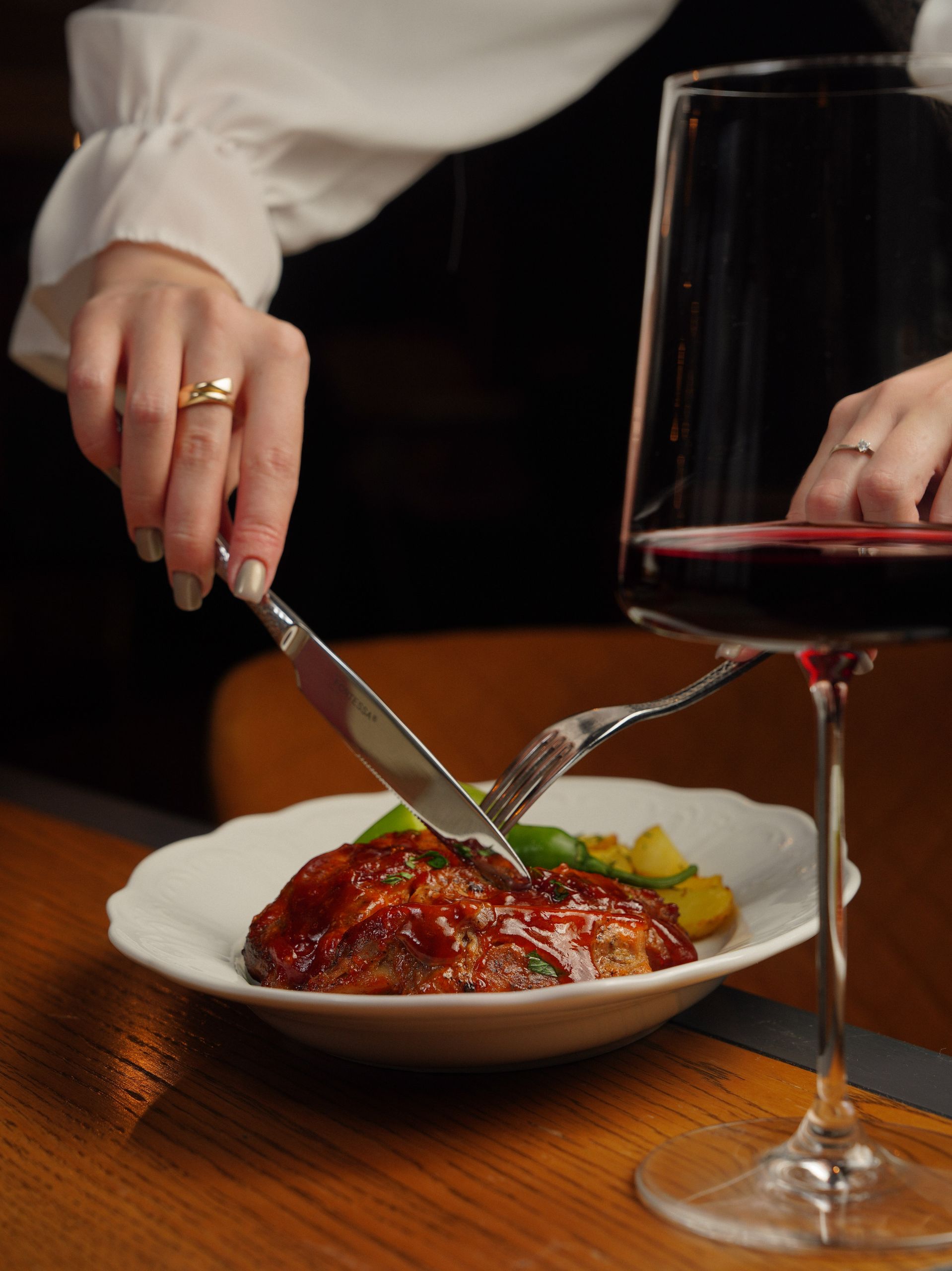 Close-up of a gourmet meal being cut, paired with red wine in an elegant setting.