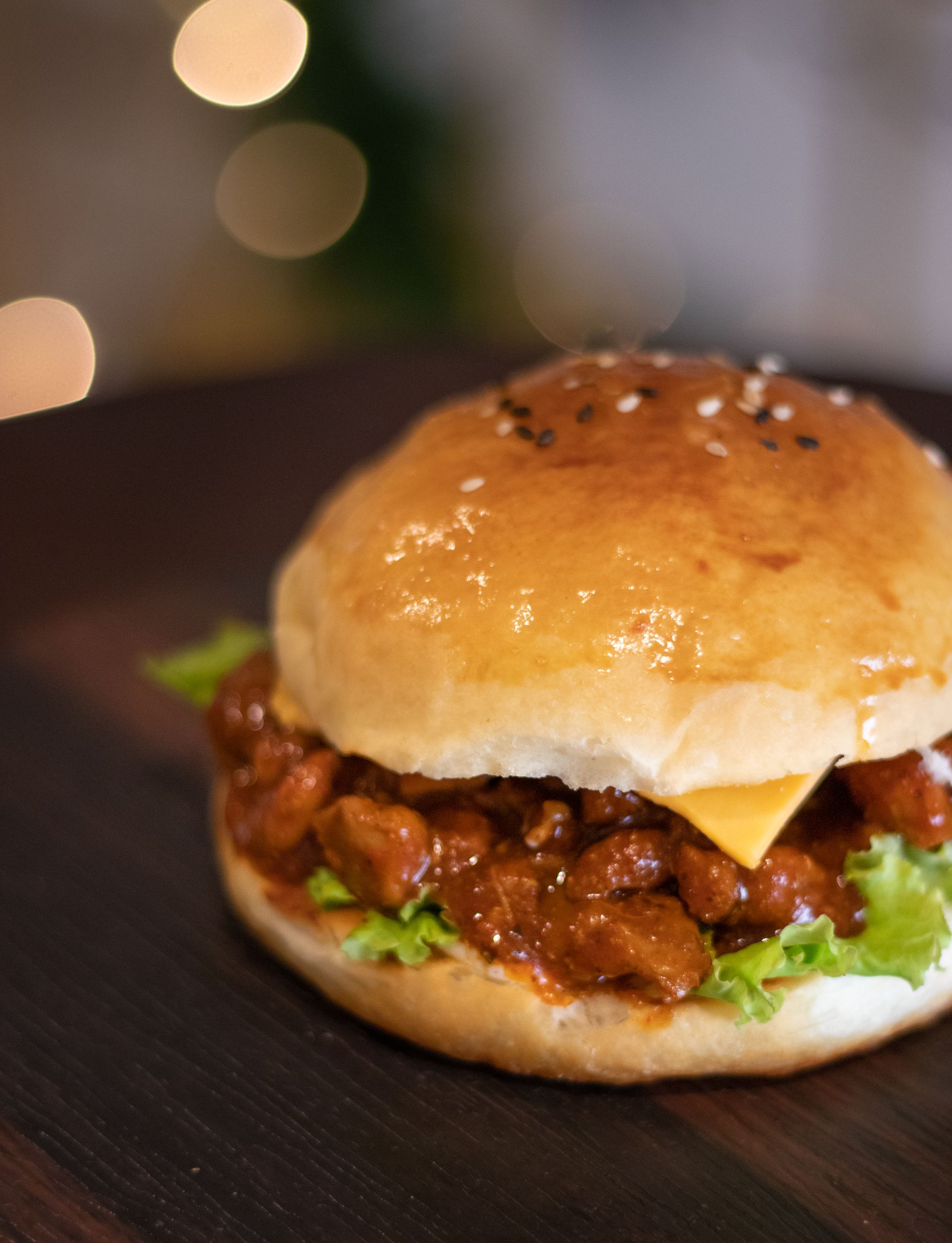 Close-up of a juicy sloppy joe burger with cheese and lettuce on a wooden board, perfect for comfort food lovers.