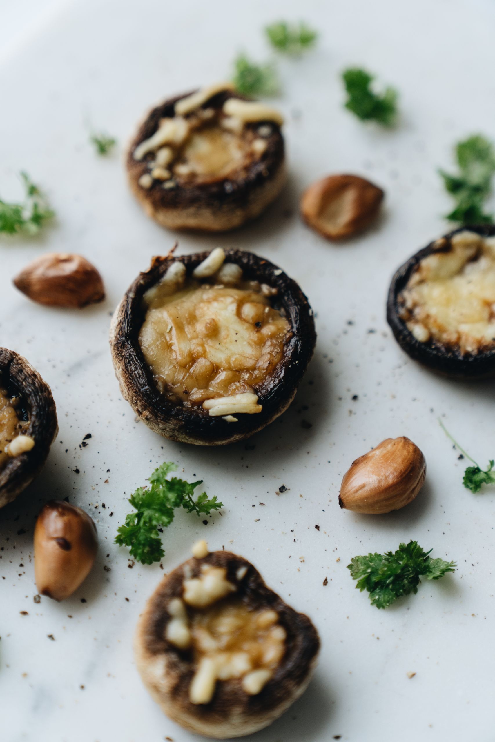 Close-up of baked mushrooms with cheese, almonds, and fresh parsley on a white surface.