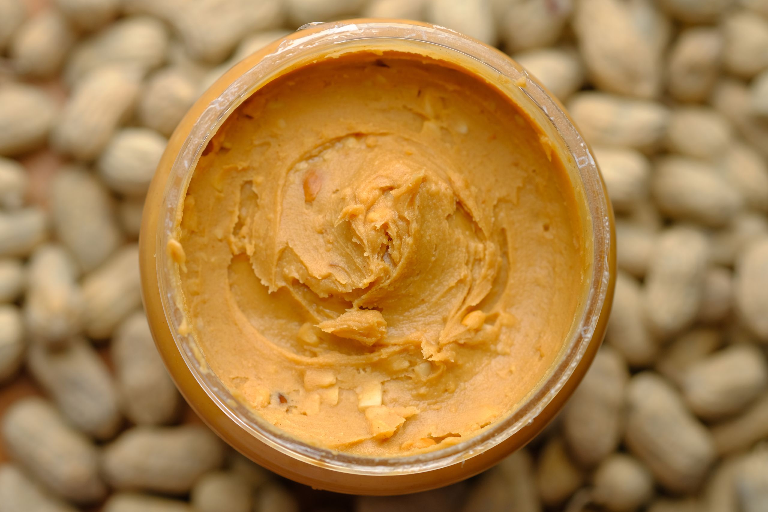 Close-up of creamy peanut butter in a glass jar surrounded by peanuts. Tasty and homemade.