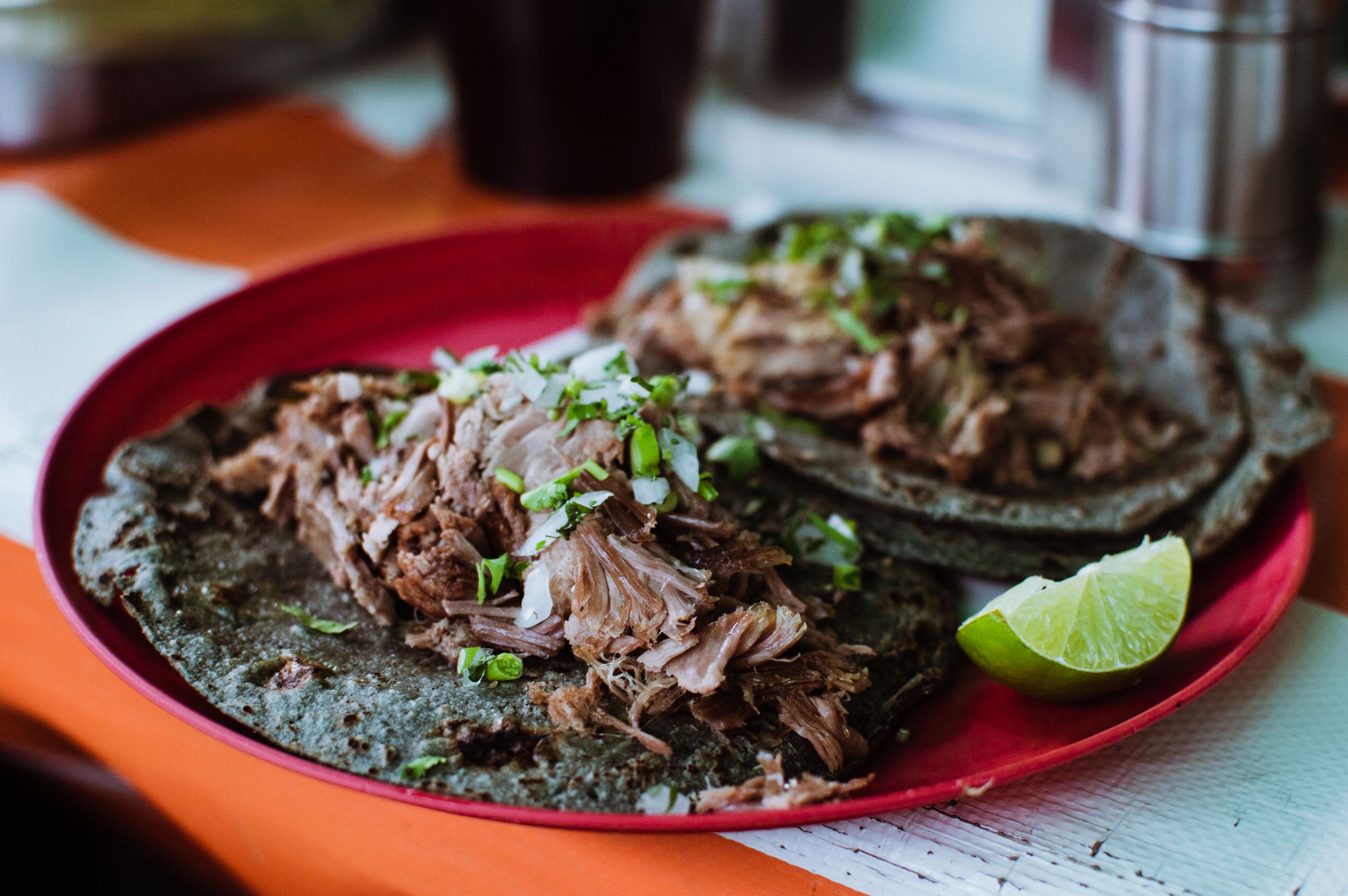Close-up of delicious barbacoa tacos on a red plate with fresh lime in Ciudad de México.