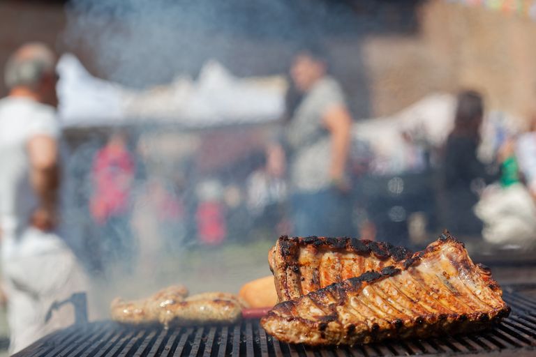 Close-up of delicious ribs sizzling on an outdoor grill with a lively background setting.