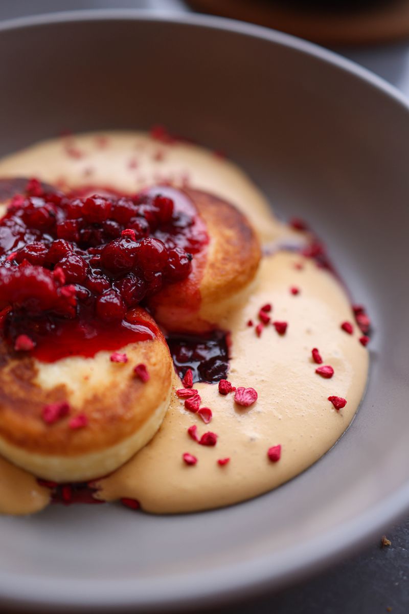 Close-up of fluffy pancakes topped with mixed berry sauce in a ceramic bowl. Perfect for brunch or dessert.
