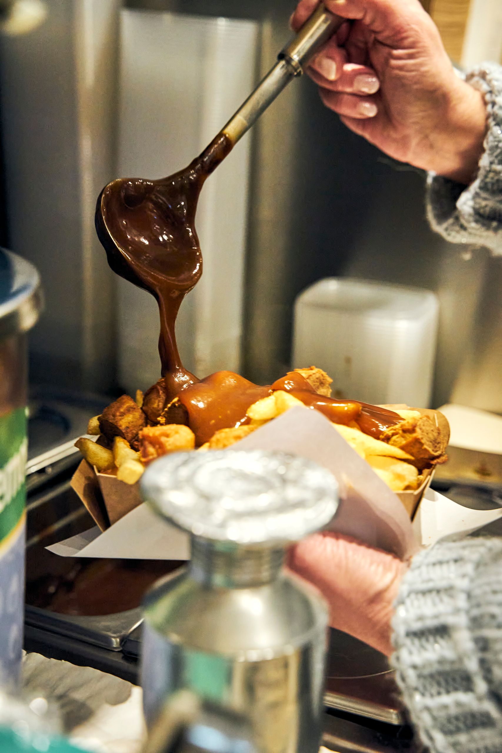 Close-up of fresh fries topped with rich gravy in an indoor setting, showcasing comfort food preparation.