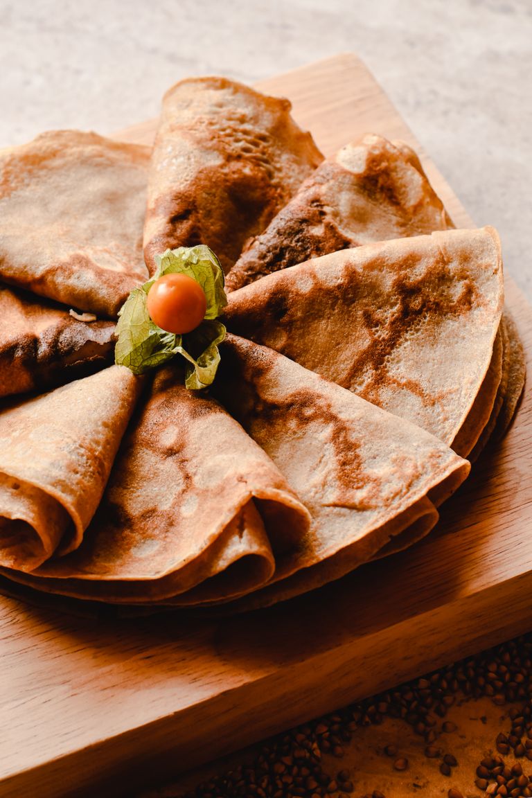 Close-up of golden brown crepes with a physalis garnish on a rustic wooden board.