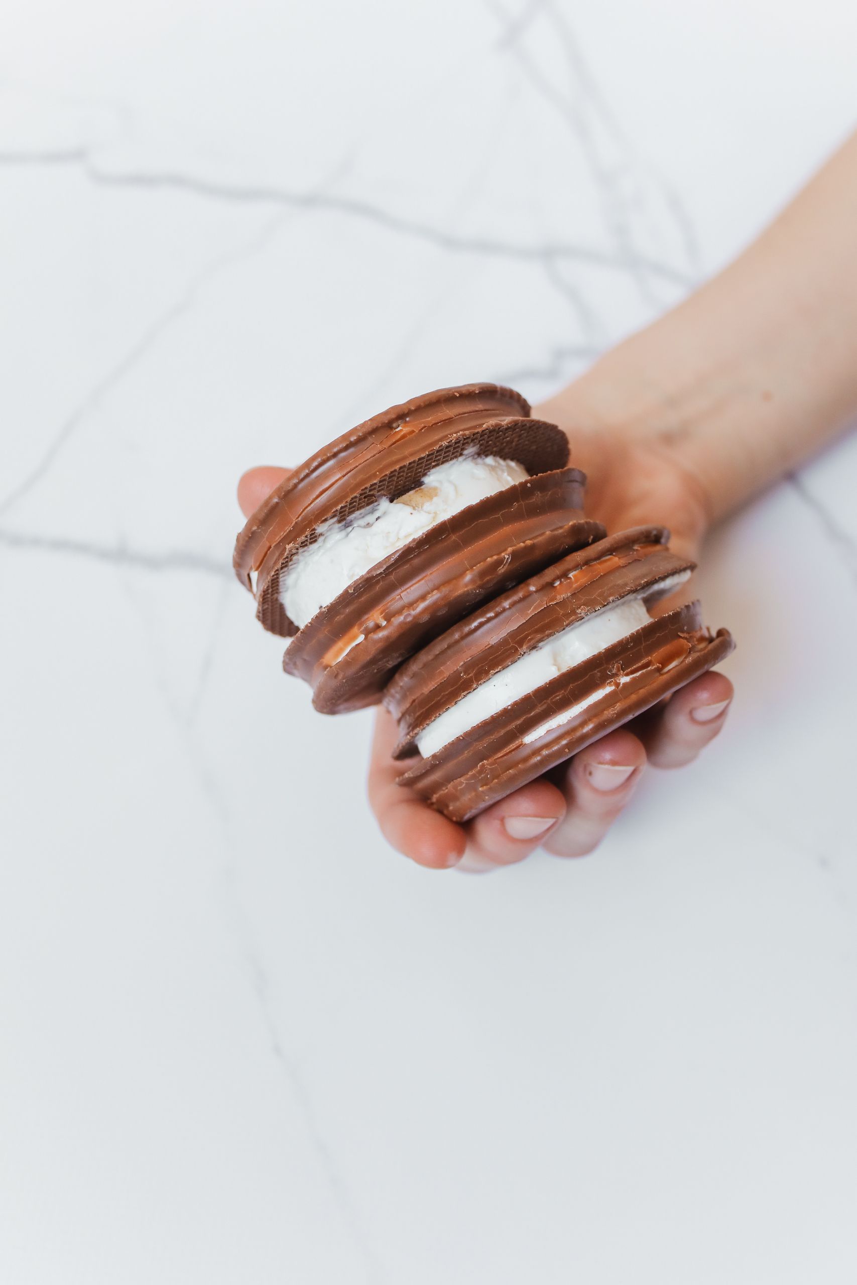 Close-up of hand holding chocolate macarons with creamy filling.