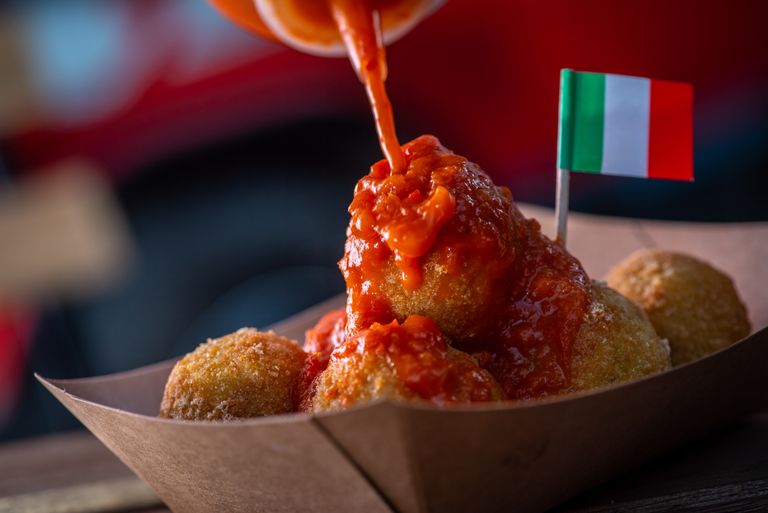 Close-up of Italian arancini drizzled with rich tomato sauce and an Italian flag.