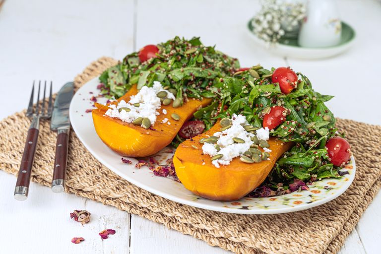 Close-up of roasted butternut squash with quinoa salad, cherry tomatoes, and feta.