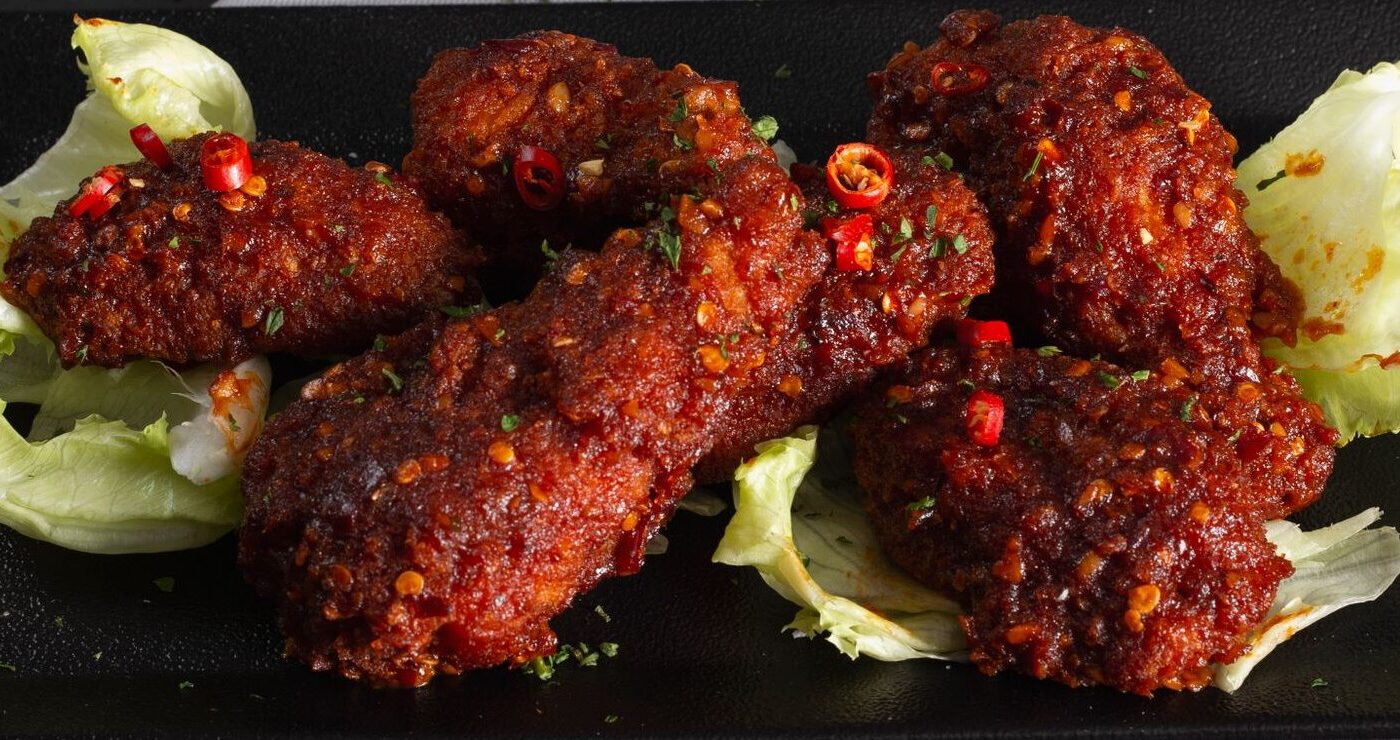 Close-up of spicy fried chicken wings on a dark plate, garnished with lettuce and herbs.