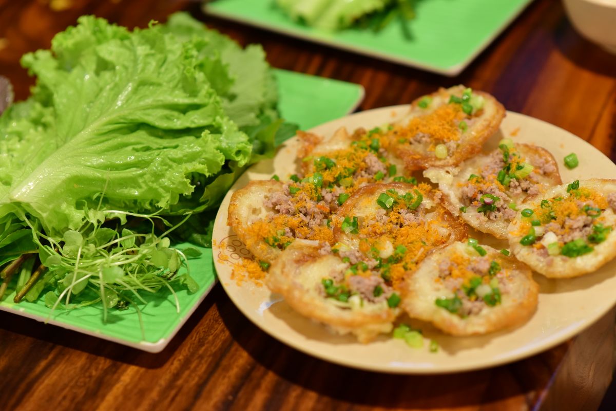 Close-up of Vietnamese b&aacute;nh khọt served with fresh lettuce on a wooden table, showcasing colorful and fresh presentation.