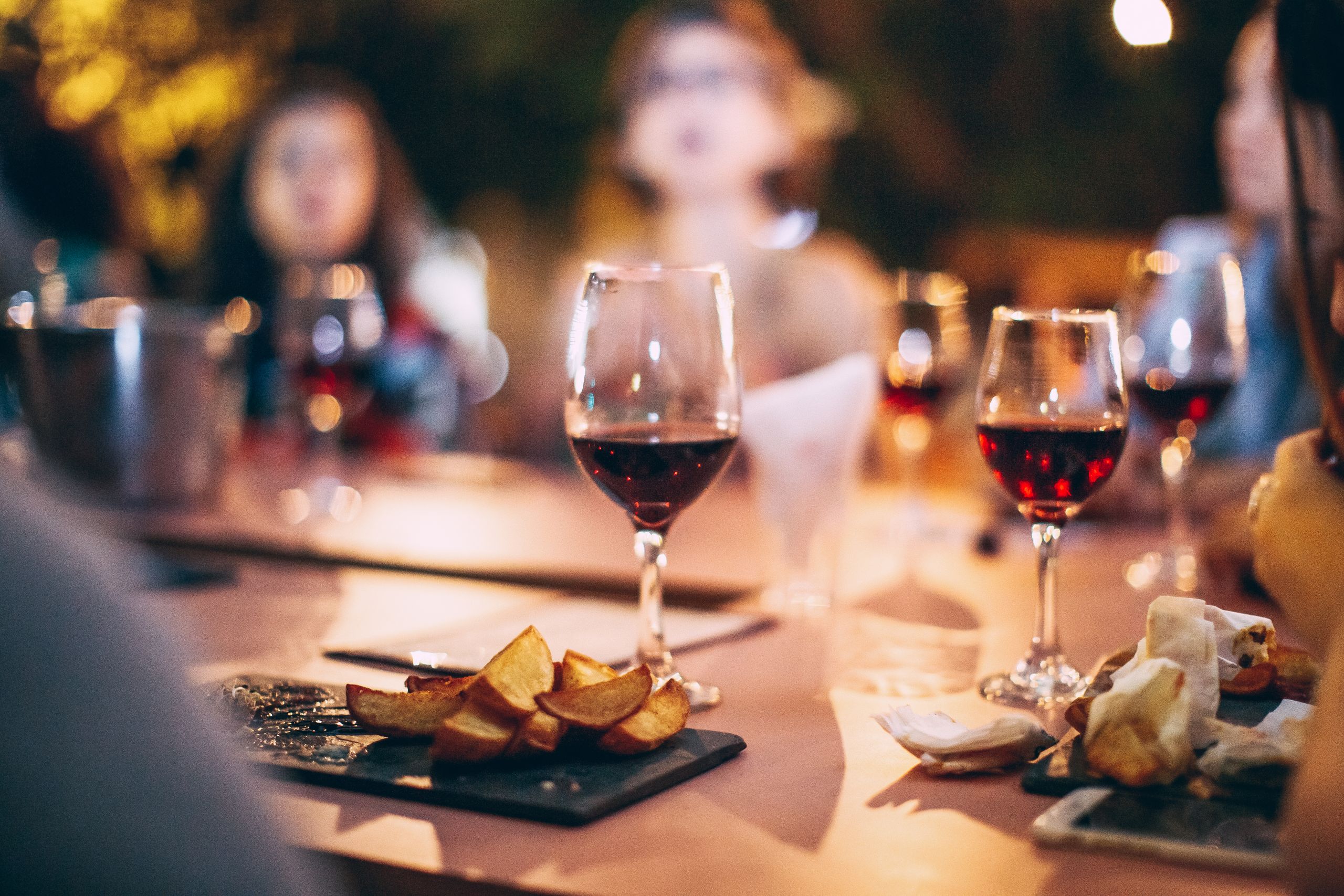 Cozy dinner party atmosphere featuring red wine, snacks, and blurred social gathering.