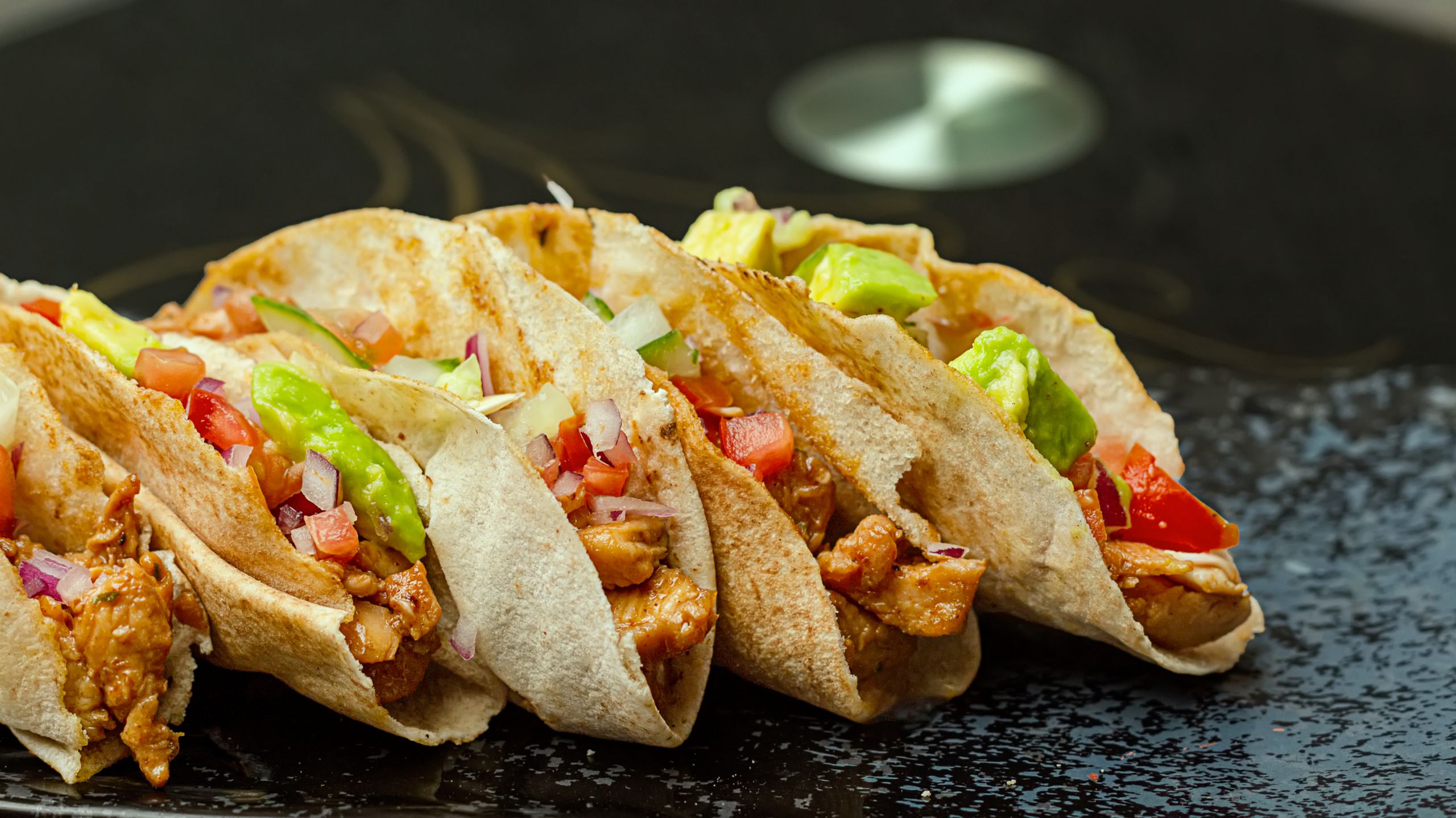 Delicious chicken tacos with avocado and fresh salsa on a black plate.