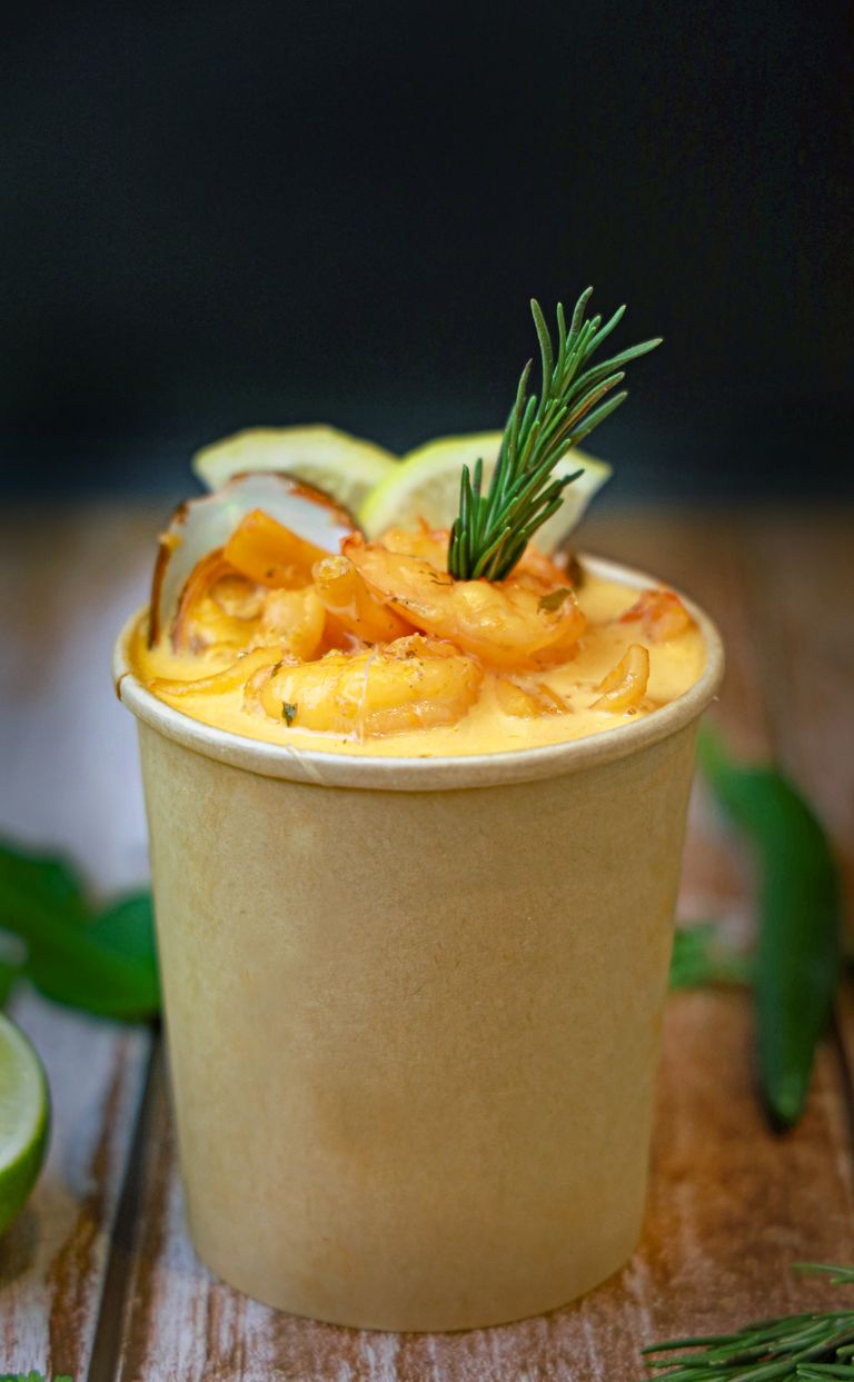 Delicious creamy seafood chowder served in a biodegradable cup garnished with shrimp and rosemary.