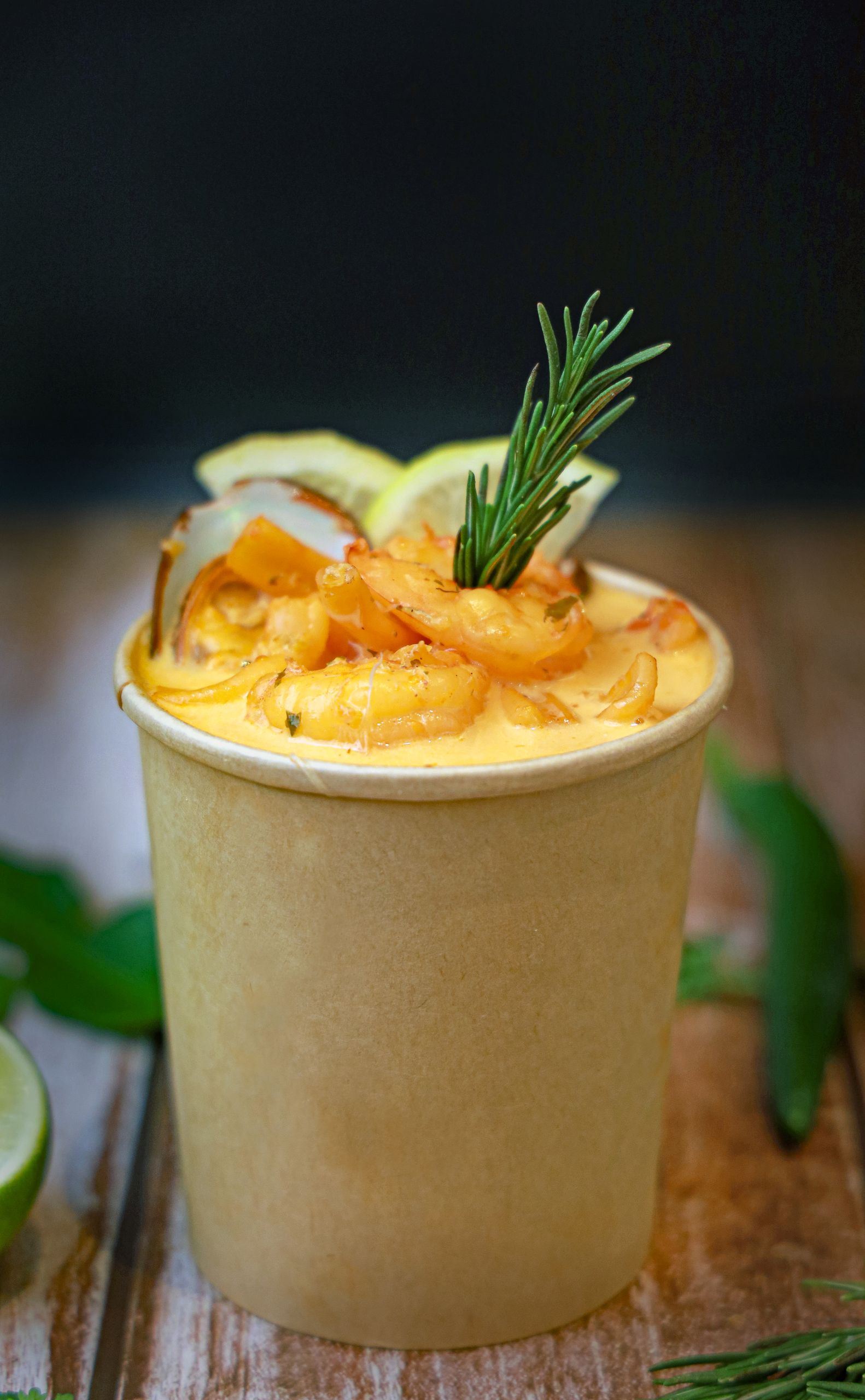 Delicious creamy seafood chowder served in a biodegradable cup garnished with shrimp and rosemary.