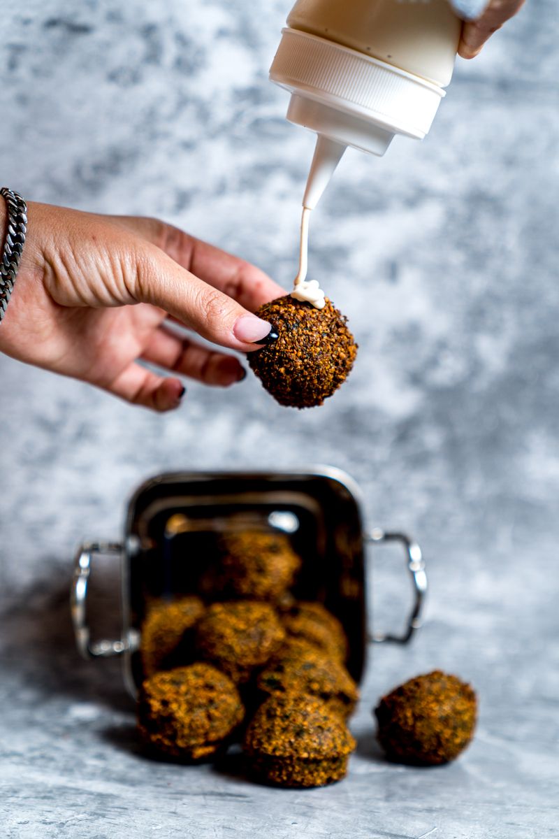 Delicious falafel being drizzled with creamy sauce, perfect for a mouth-watering meal.