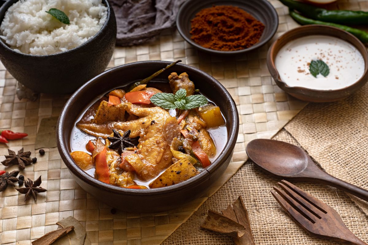 Delicious Filipino Chicken Afritada with rice, spices, and herbs in a high-angle view, showcasing vibrant flavors.