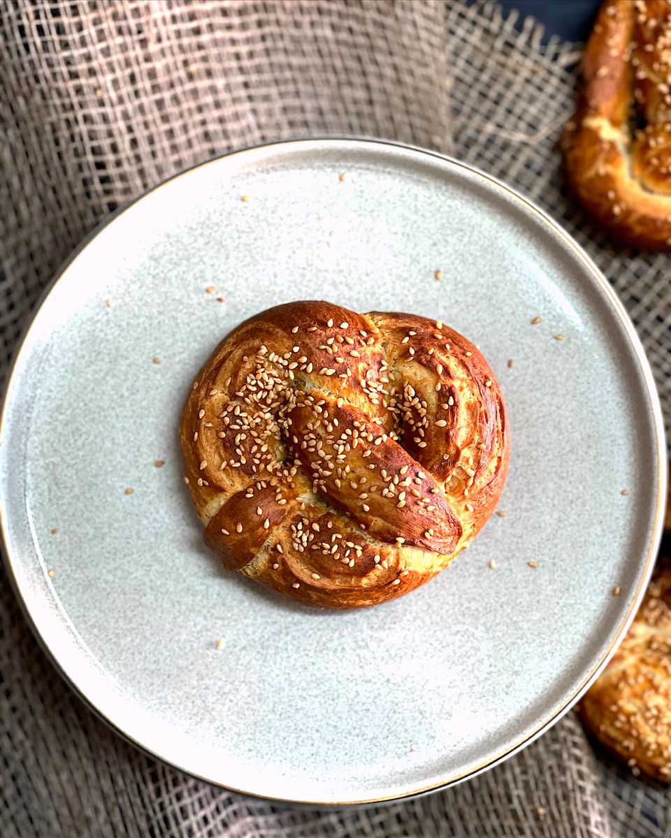 Delicious freshly baked soft pretzel topped with sesame seeds on a plate.