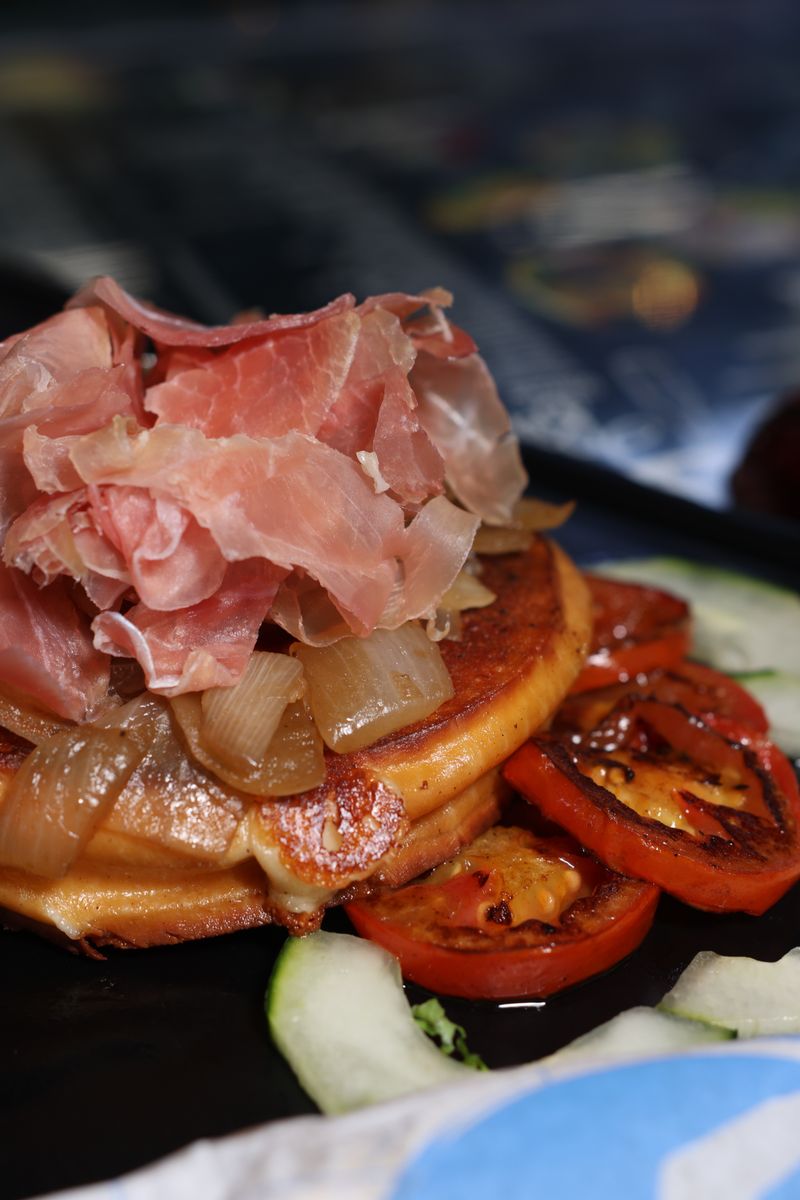 Delicious gourmet breakfast featuring pancakes topped with jamon serrano and roasted vegetables.