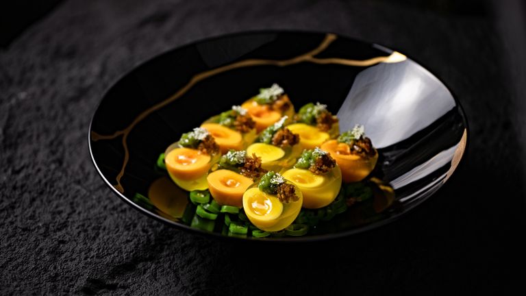 Delicious gourmet dish featuring artistically plated eggs with fresh greens on a decorative black plate.