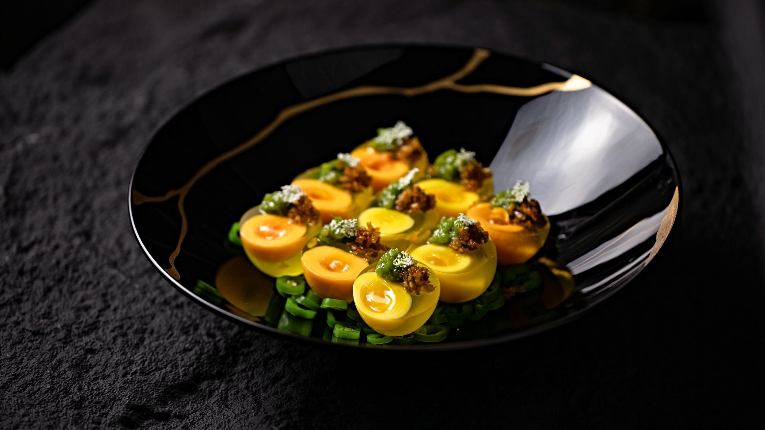 Delicious gourmet dish featuring artistically plated eggs with fresh greens on a decorative black plate.