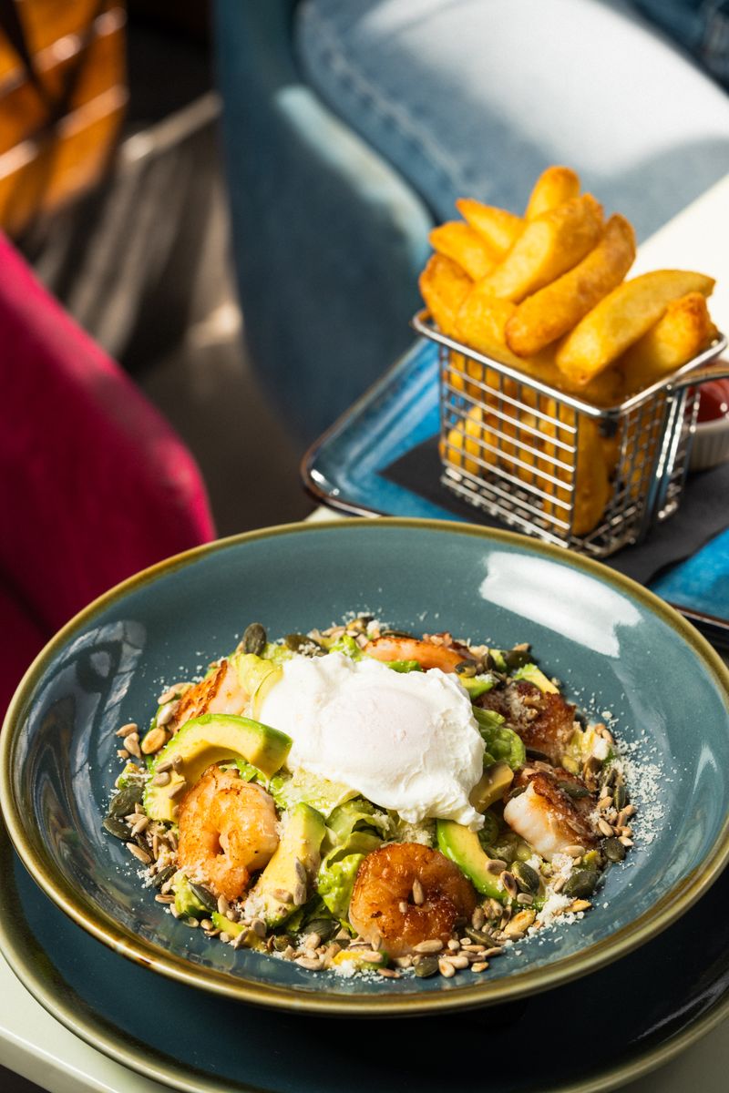Delicious gourmet salad with shrimp, avocado, and poached egg, served with fries.