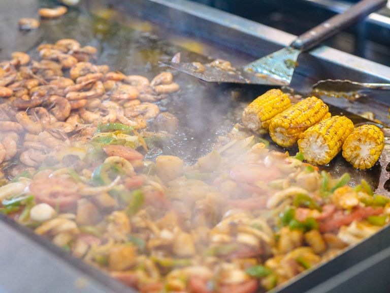 Delicious grilled prawns and corn with vegetables being cooked on a street food grill.