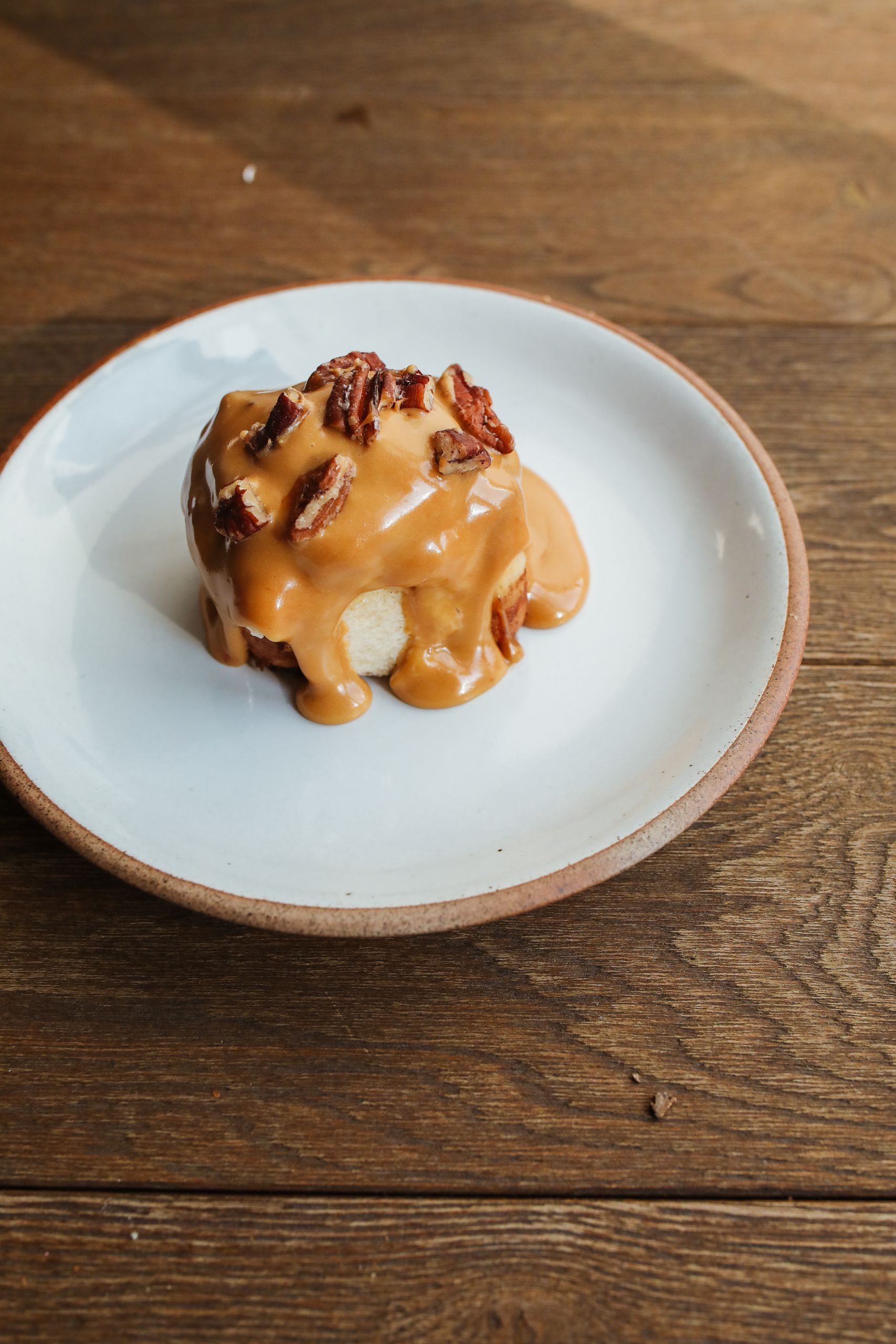 Delicious sticky toffee pudding topped with pecans, served on a rustic wooden table.