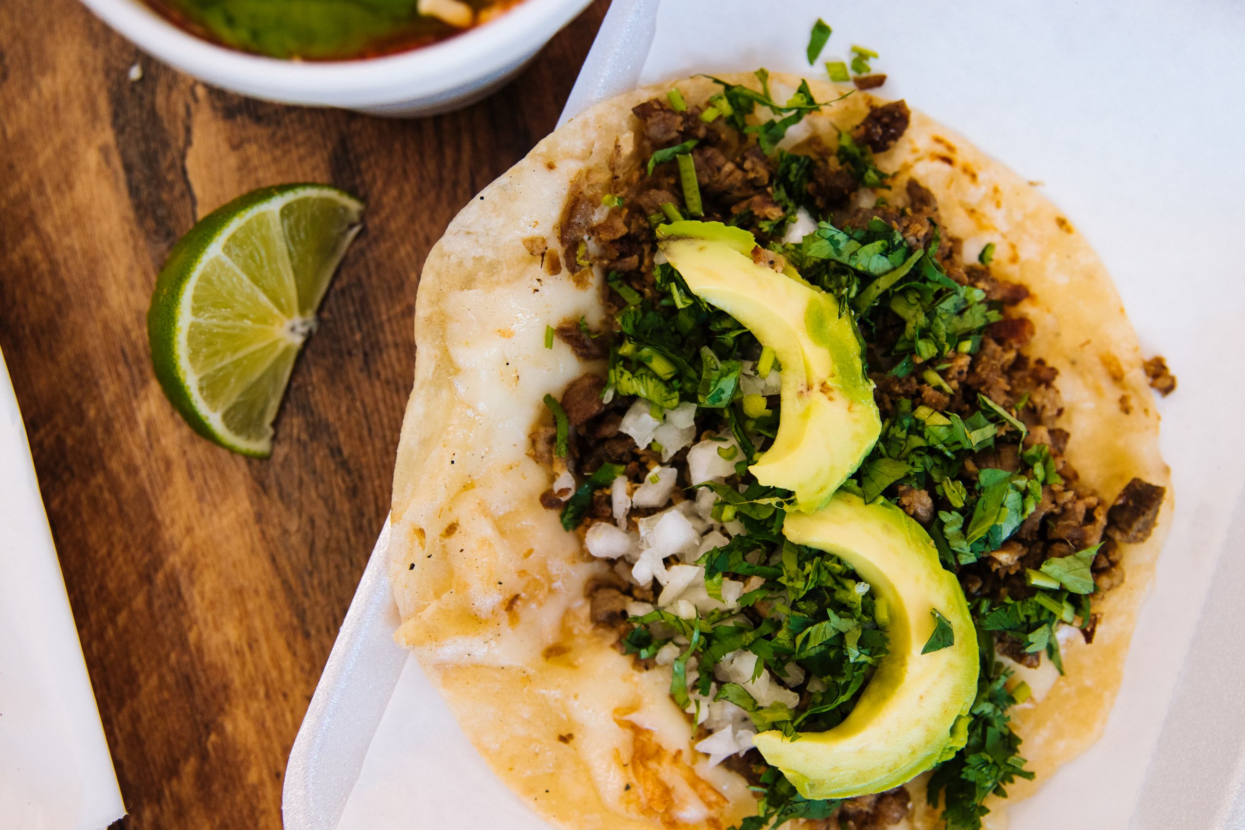 Delicious taco with avocado, cilantro, and lime slice shot from above on wooden table.