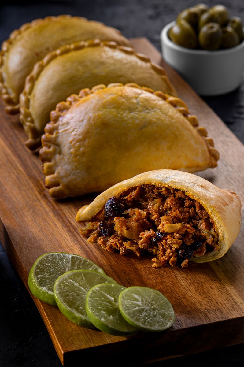 Freshly baked Peruvian empanadas filled with beef, served with lime slices on a wooden board.