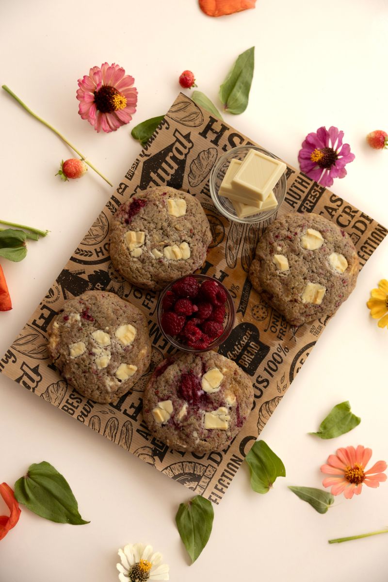 Freshly baked raspberry white chocolate cookies surrounded by colorful flowers and leaves, perfect for a vibrant table setting.