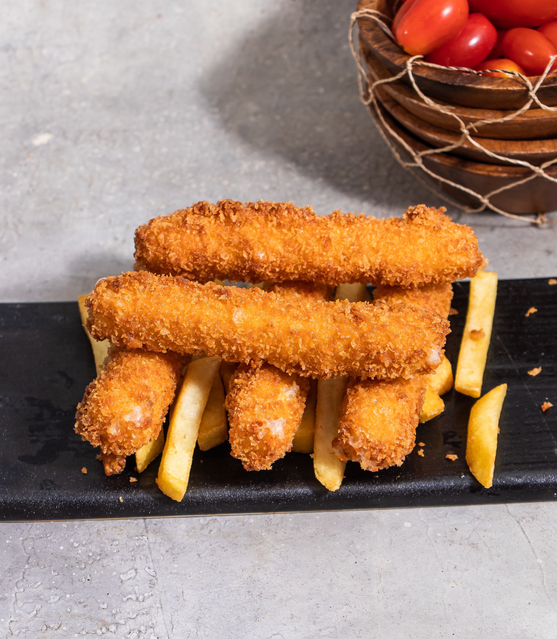 Golden brown fish sticks served with fries on a slate plate, perfect for a delicious meal.