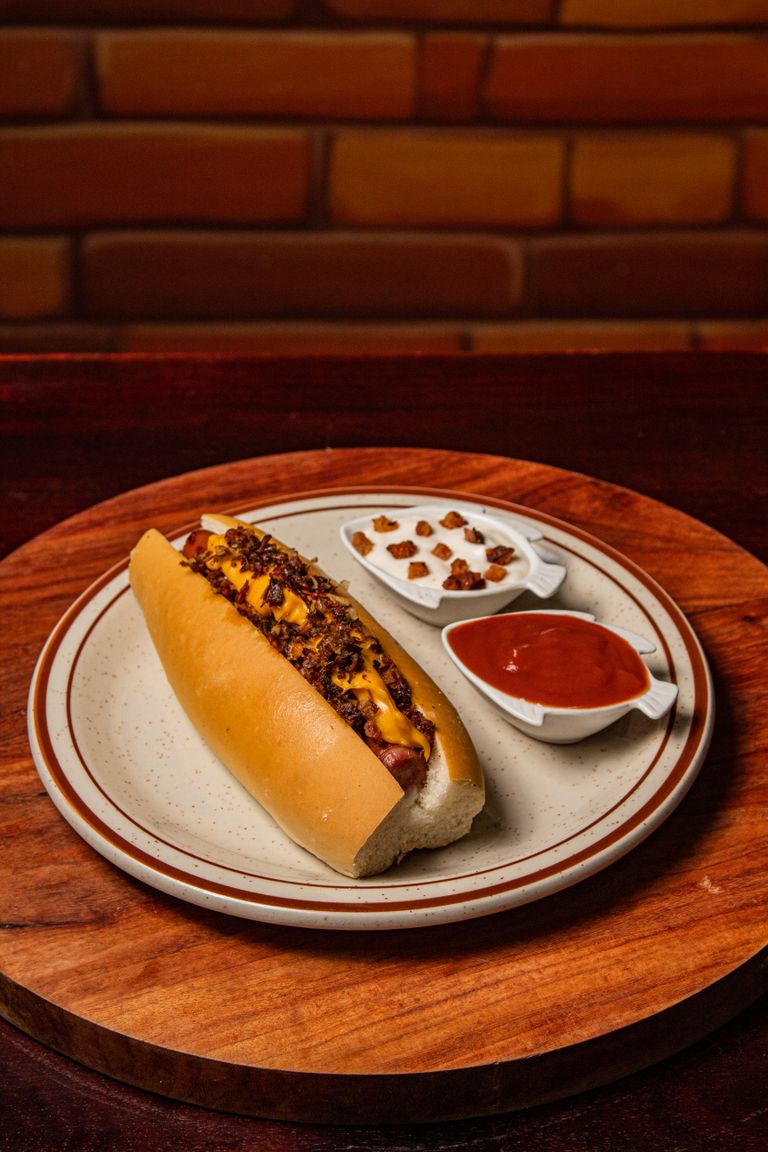 Gourmet hot dog served on a plate with relish and ketchup in a cozy setting.