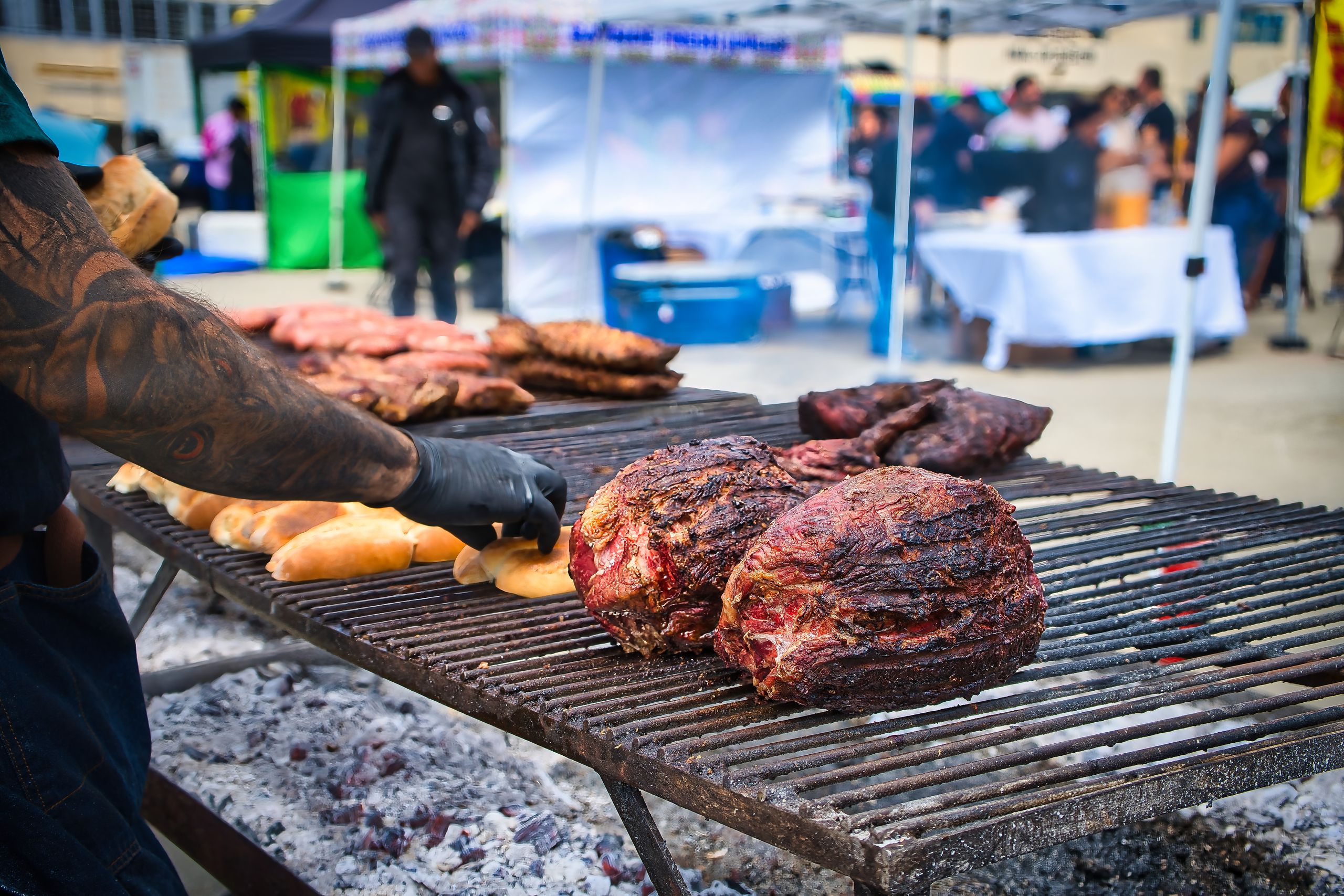 Grilled meat and bread on a barbecue grill at an outdoor food market.