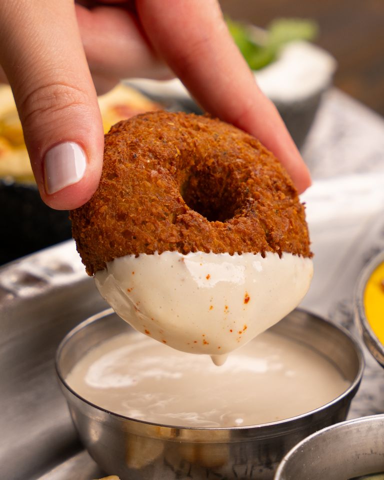 Hand holding a falafel being dipped into a creamy sauce for a tasty snack.