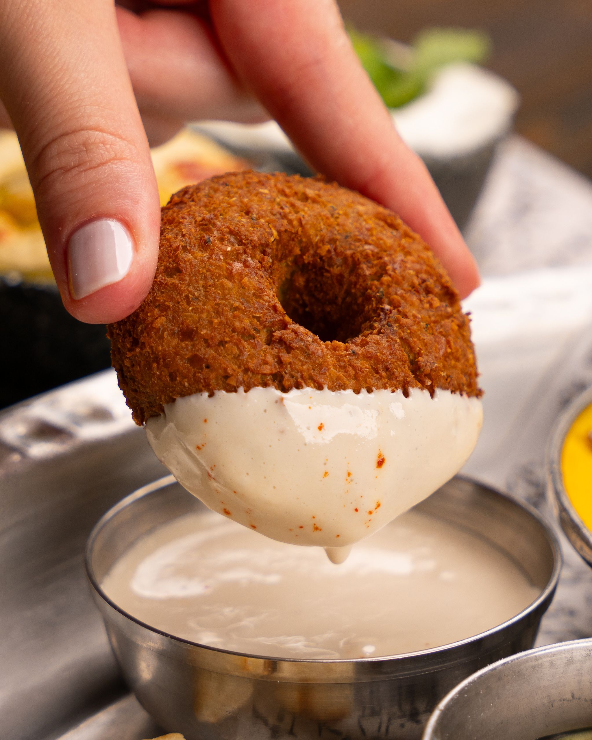 Hand holding a falafel being dipped into a creamy sauce for a tasty snack.