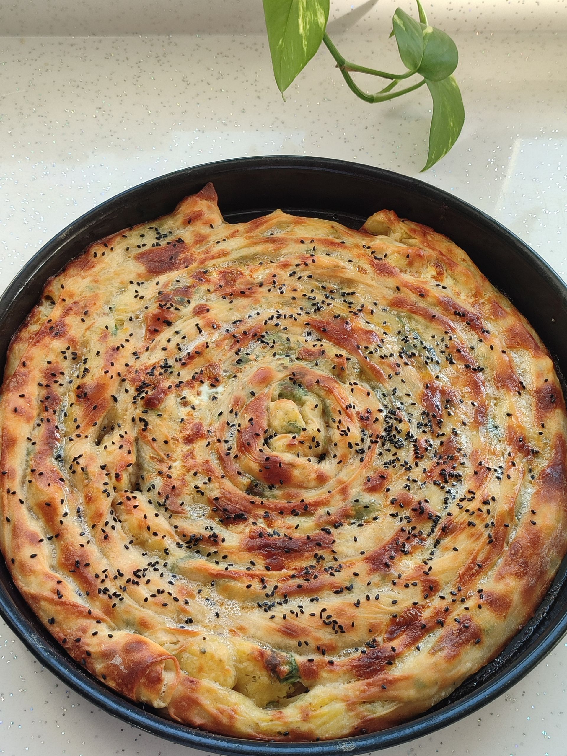 Hot spiral-shaped savory pie topped with seeds, freshly baked to golden perfection in a round pan.