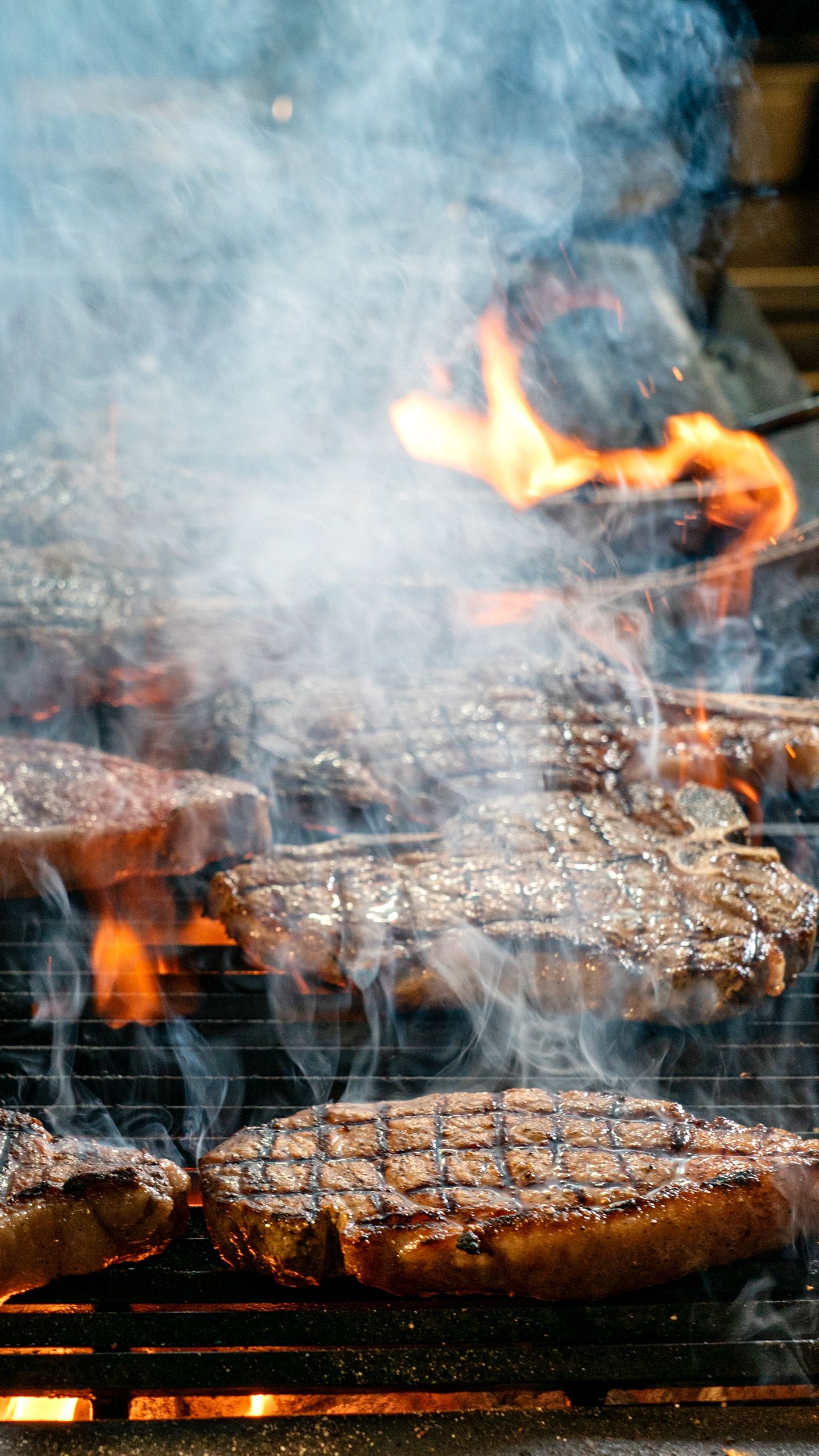Juicy steaks grilling over open flames with smoke on a barbecue.