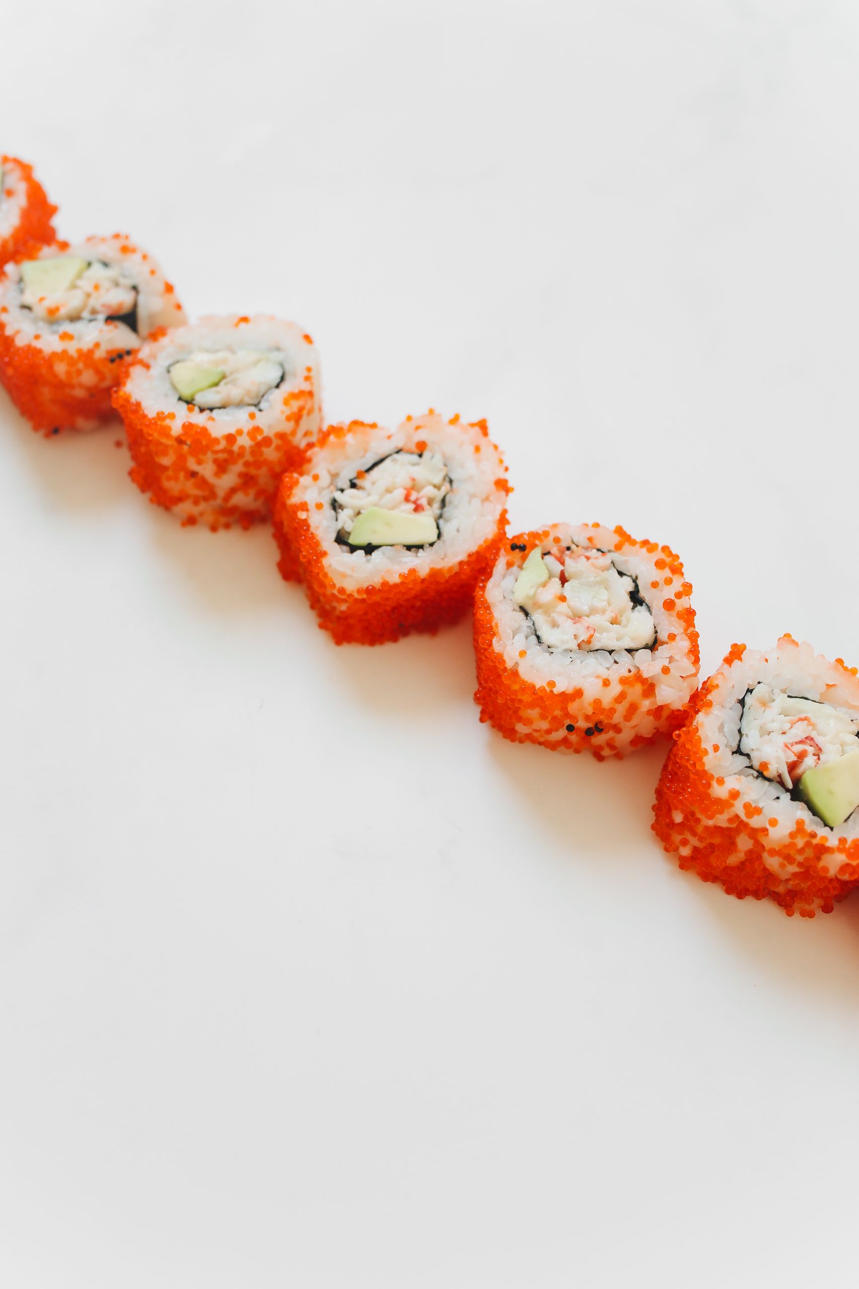 Line of colorful California sushi rolls with vibrant orange tobiko, avocado, and crab.