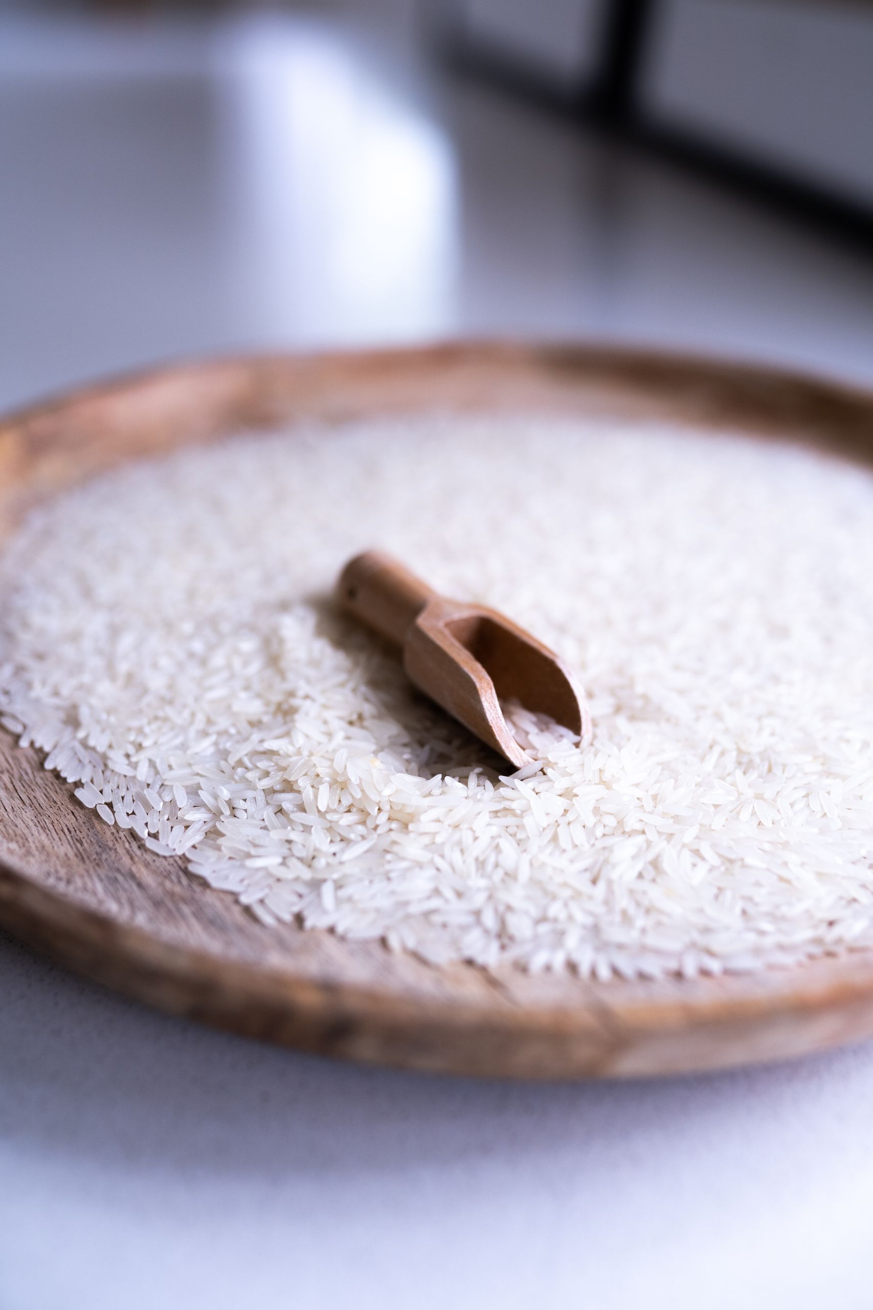 Minimalist image of uncooked white rice with a wooden scoop on a tray. Perfect for culinary themes.
